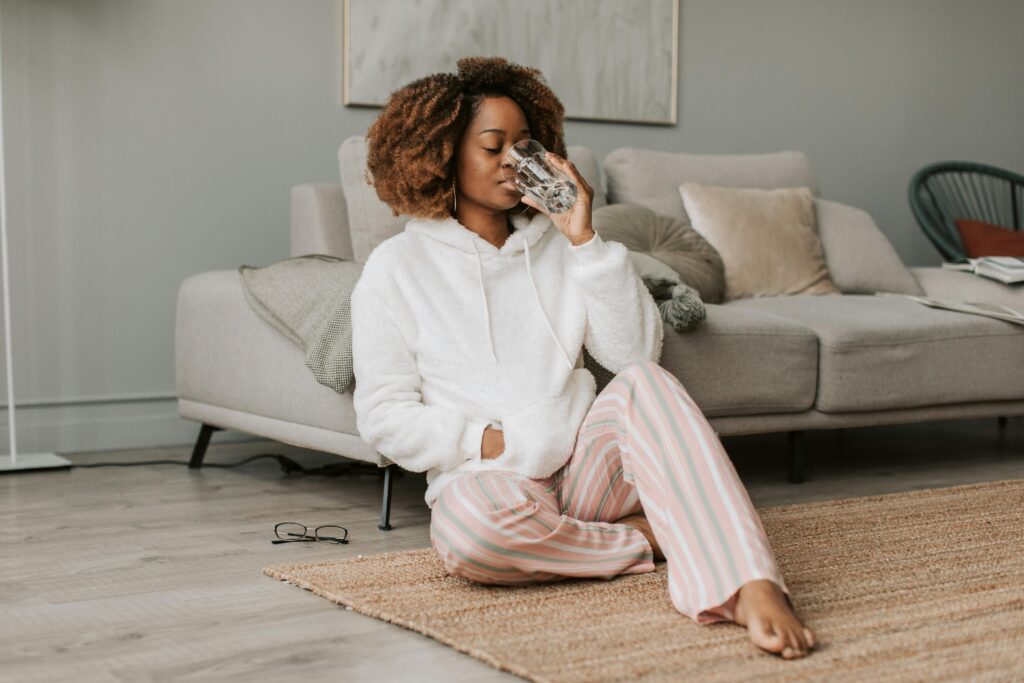 Woman sitting at home drinking water in a calm setting, representing self-care and understanding midlife menopause symptoms
